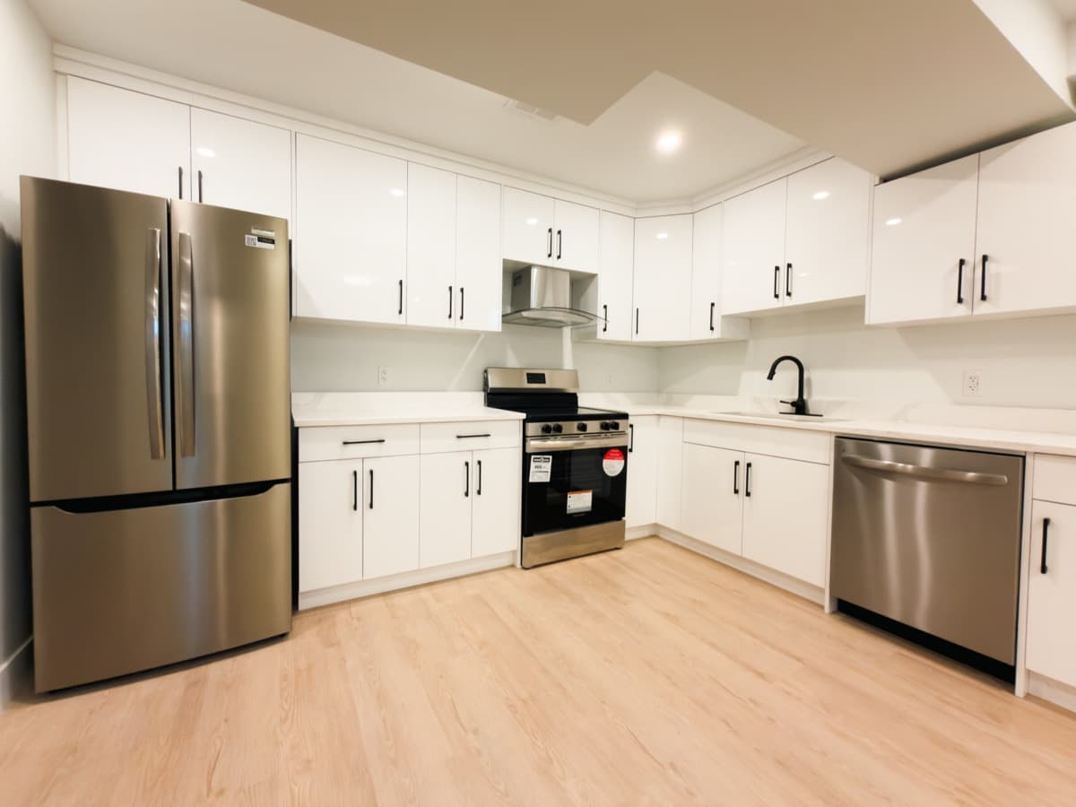 White gloss kitchen with a stainless French-door fridge, range, hood fan and dishwasher on light plank flooring