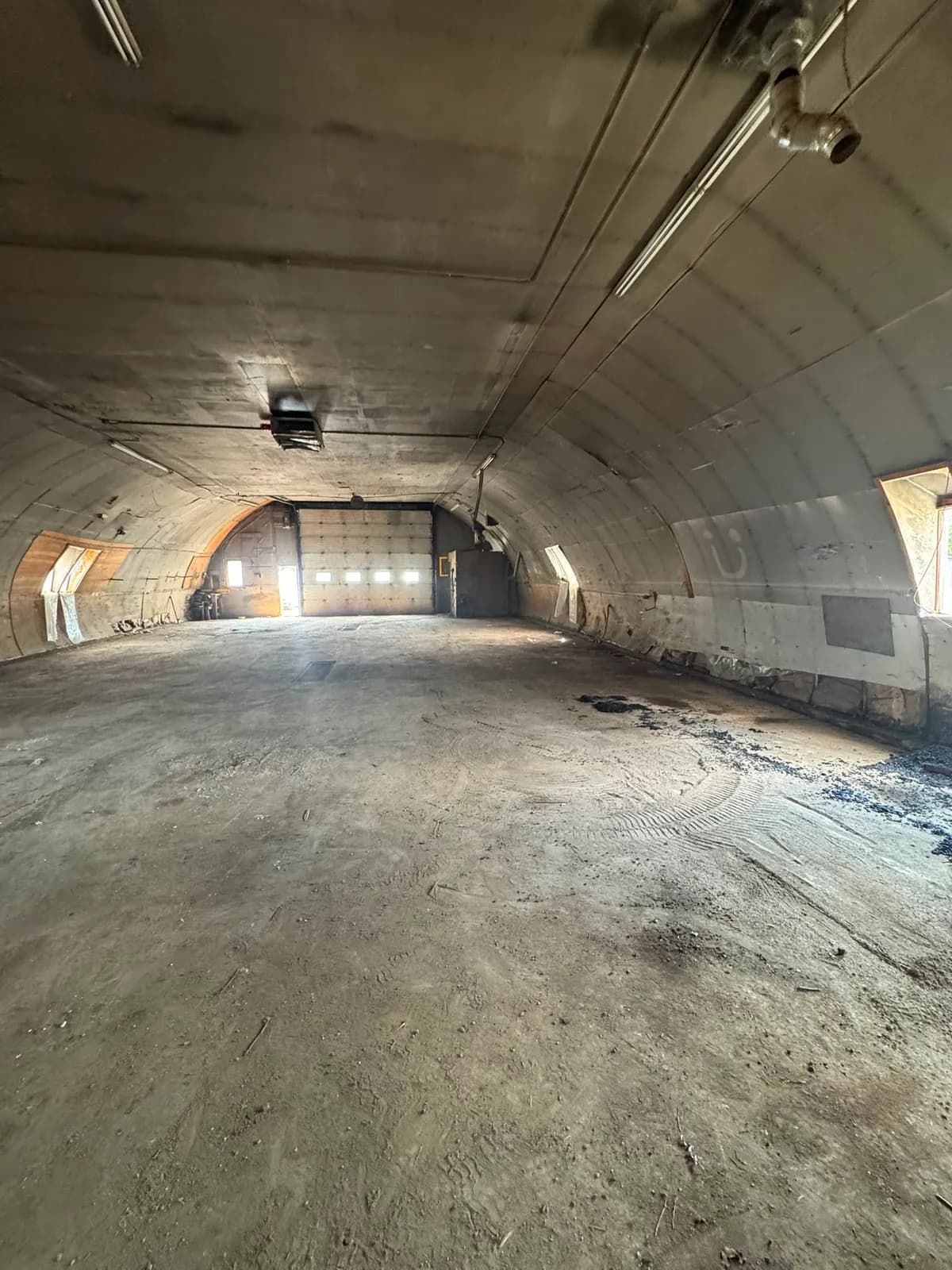 Inside an arched steel storage building, with a wide concrete floor running to an overhead door at the far end