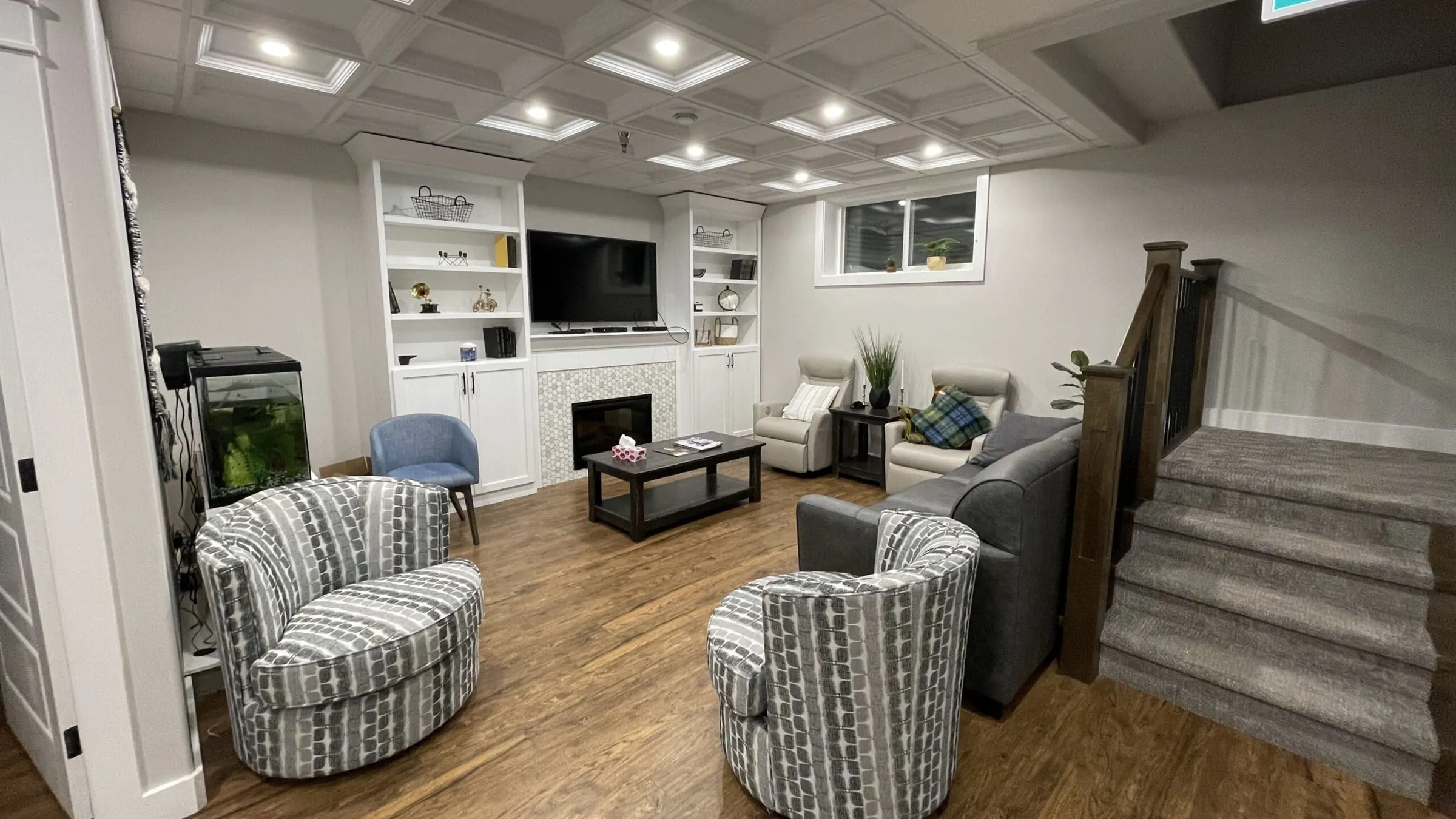 Care home lounge with a coffered ceiling, built-in shelving around a fireplace, swivel armchairs and a carpeted stair