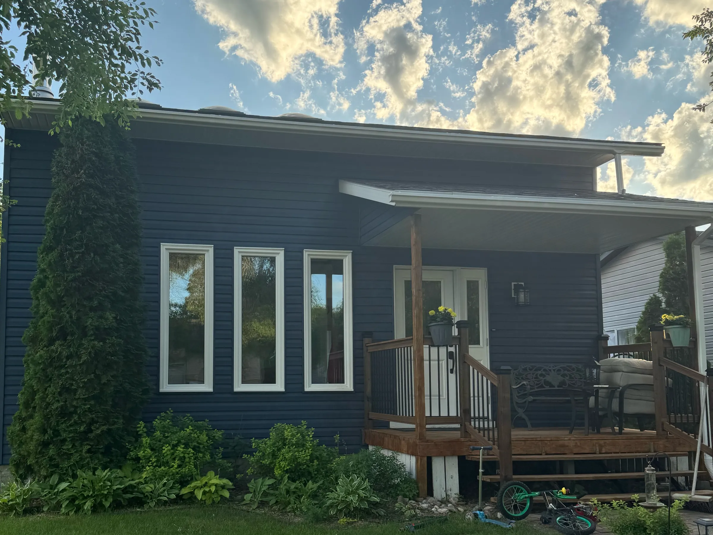 Navy-sided house with three tall windows and a covered front porch under a cloudy sky